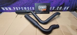 Two matte black exhaust pipes are displayed on a cardboard surface with a Cerakote PB sign and a purple and black background featuring a web address.