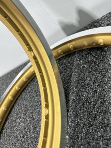 Close-up of two metallic rim sections, one gold and one silver, resting on a textured gray carpet near a white wall.