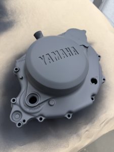 Matte gray Yamaha motorcycle engine cover resting on a beige surface, with visible embossed branding and bolt holes.